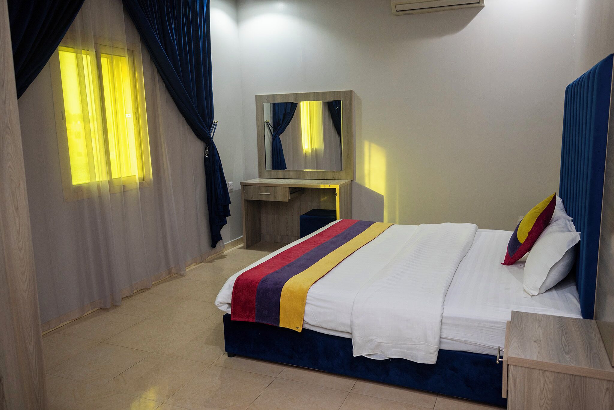 A bedroom with a bed, a desk, a mirror, and curtains.