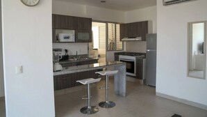 Cocina moderna con armarios de madera oscura, encimera de granito, microondas integrado, estufa y refrigerador. Hay dos taburetes de bar y un reloj en la pared.