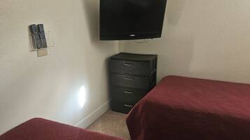 Une chambre avec deux lits, un téléviseur fixé au mur, une petite armoire et un tableau encadré.