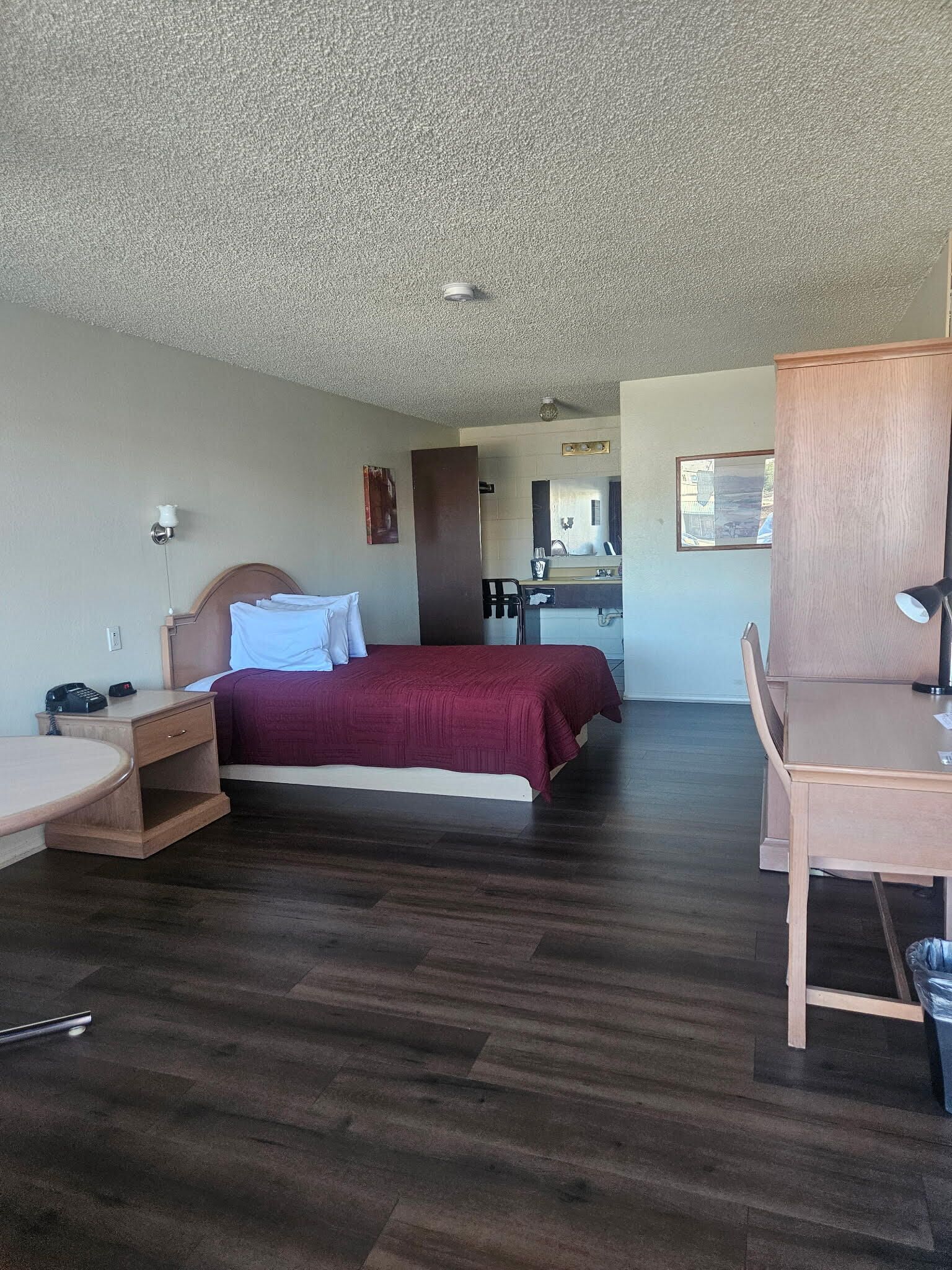 A hotel room with a bed, a desk, a chair, a small table, a mirror, and a window.