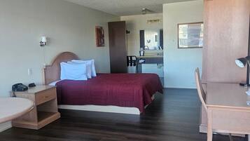 A hotel room with a bed, a desk, a chair, a small table, a mirror, and a window.