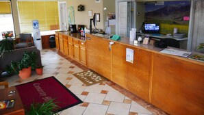 A reception area with a wooden counter, a water dispenser, a television, and a large window. - Camaray Motel (Oroville)