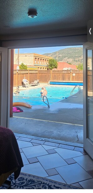 A view of a swimming pool area with a wooden fence, a person sitting on a chair, and a building in the background. - Camaray Motel (Oroville)