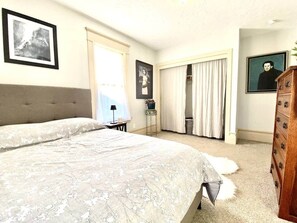 Un dormitorio con una cama grande, un aparador, una ventana con cortinas y una puerta.