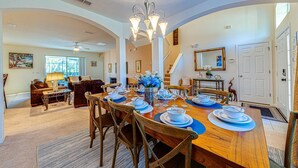 Une salle à manger spacieuse, avec une grande table en bois dressée pour six personnes, entourée de chaises en bois. Un lustre est suspendu au-dessus de la table, et un escalier mène à un autre niveau.