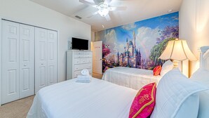 Une chambre d’hôtel avec deux lits, un ventilateur de plafond, un téléviseur posé sur une commode et une fresque représentant un château.
