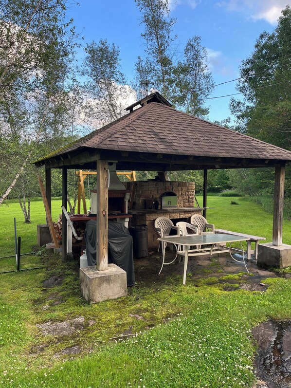 Ett rustikt utomhuskök med en stenmur, ett träbord och en överbyggd sittplats.