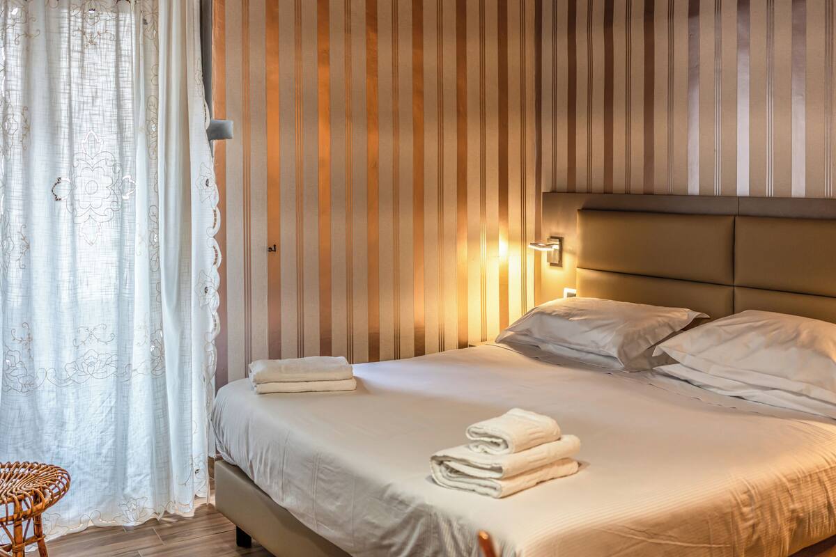 A neatly made bed with pillows and folded towels, a bedside lamp, and a striped wall.