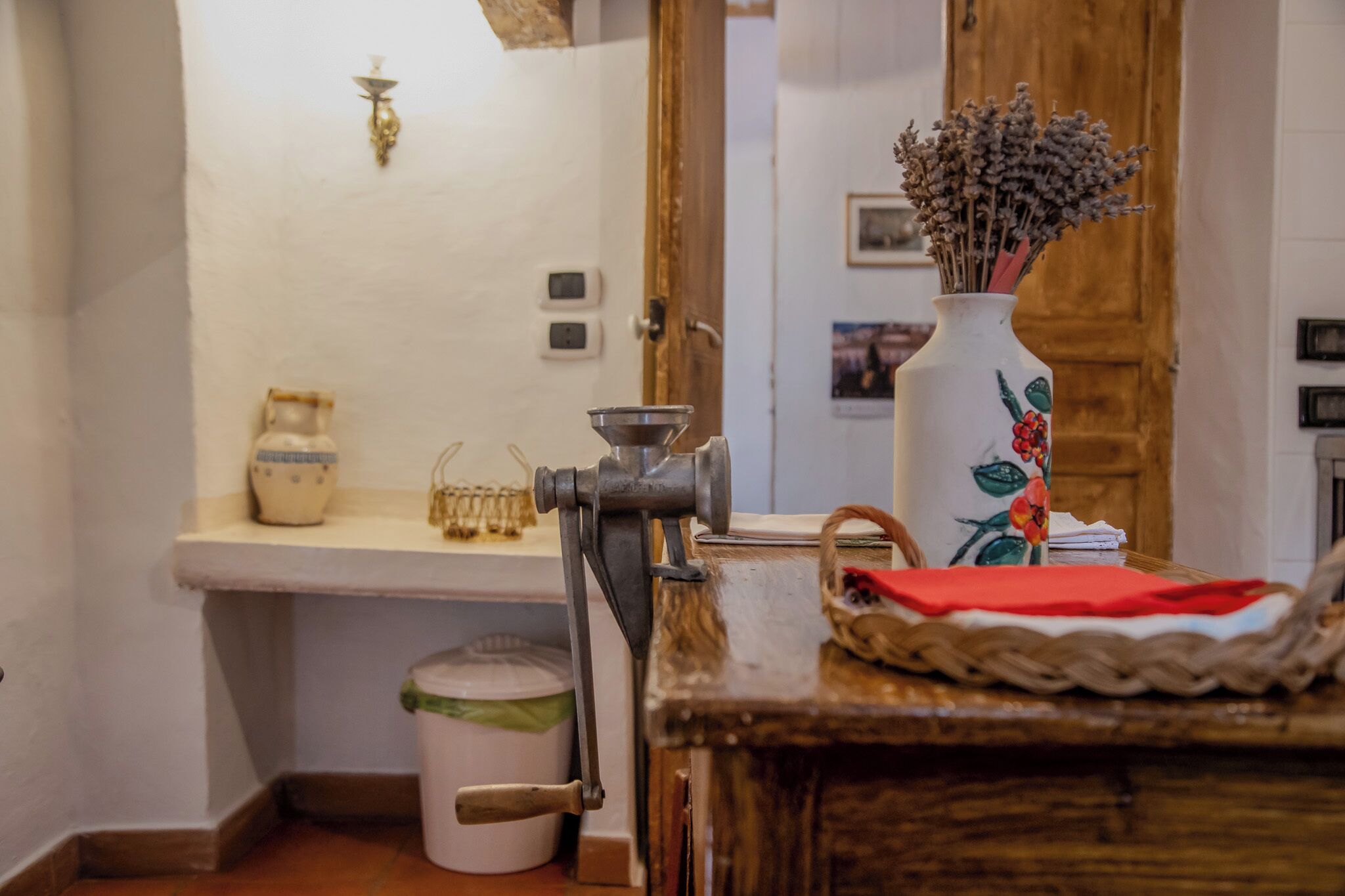 A rustic kitchen with a vintage meat grinder, a ceramic vase with dried flowers, and a wooden table.