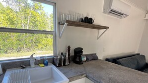 A compact kitchenette with a sink, countertop, and a window overlooking greenery.