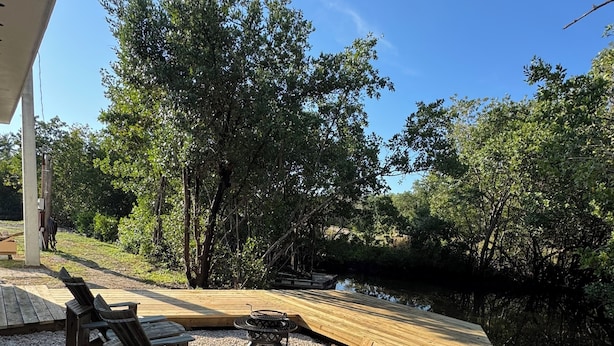 A wooden deck with outdoor seating and a grill, surrounded by trees and a body of water.