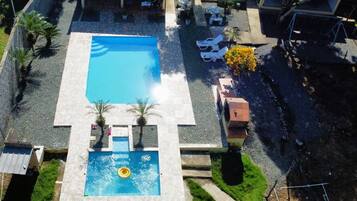 An aerial view of a hotel with a central swimming pool, surrounded by lounge chairs and palm trees.