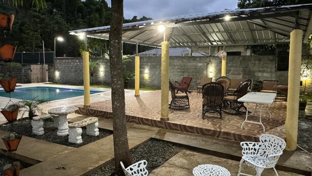 Un espace extérieur aménagé avec une terrasse, une piscine, des coins salon et une partie couverte avec éclairage.