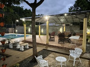 Un espace extérieur aménagé avec une terrasse, une piscine, des coins salon et une partie couverte avec éclairage.