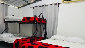 Une chambre de dortoir avec des lits superposés, du linge de lit blanc et une couverture rouge ornée de motifs en forme de cœurs noirs.
