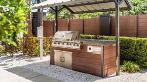 Un espace barbecue extérieur comprenant un gril, un coin salon couvert et une clôture en bois.