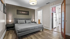 Une chambre moderne avec un grand lit, une œuvre d’art accrochée au mur, un luminaire au plafond et un plancher en bois.