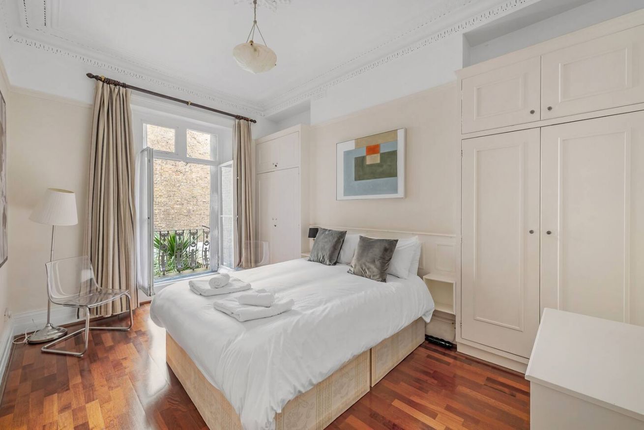 A bedroom with a large bed, a chair, a bedside table, and a wardrobe.