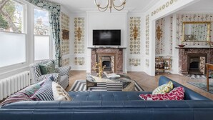 A spacious living room with a fireplace, a television, and a large window. - Blossom House New 3Bed house in Barons Court (Greater London)