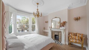 A bedroom with a large bed, a fireplace, a mirror, and a window with curtains. - Blossom House New 3Bed house in Barons Court (Greater London)