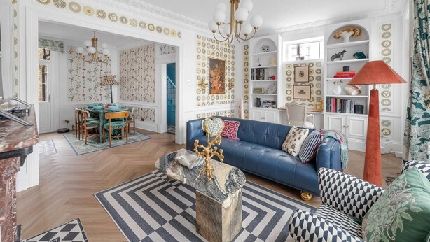 A spacious living room with a blue sofa, patterned rugs, and a chandelier. - Blossom House New 3Bed house in Barons Court (Greater London)