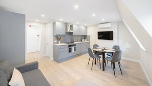 A modern kitchen with a central island, built-in oven, and a dining area with a round table and four chairs. - New 1Bed with AC near Portobello (Greater London)