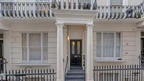 A two-story townhouse with a central entrance flanked by two columns, a black front door, and a balcony with black wrought iron railings. - New 1Bed with AC near Portobello (Greater London)