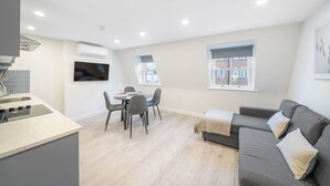 A modern apartment with a kitchen, dining area, and living room. It features a flat-screen TV, a sofa, and a window with a city view. - New 1Bed with AC near Portobello (Greater London)