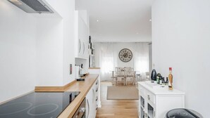 A modern kitchen with a black induction cooktop, wooden cabinets, and a white countertop. - New 2Bed with Air Con in Kensington (London)