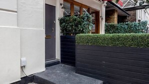 A modern building with a white exterior, a wooden door, and a black planter with green foliage. - New 2Bed with Air Con in Kensington (London)