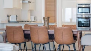 A modern kitchen with white cabinetry, a built-in oven, and a dining area with brown leather chairs. - New 3Bed in Knightsbridge (Greater London)