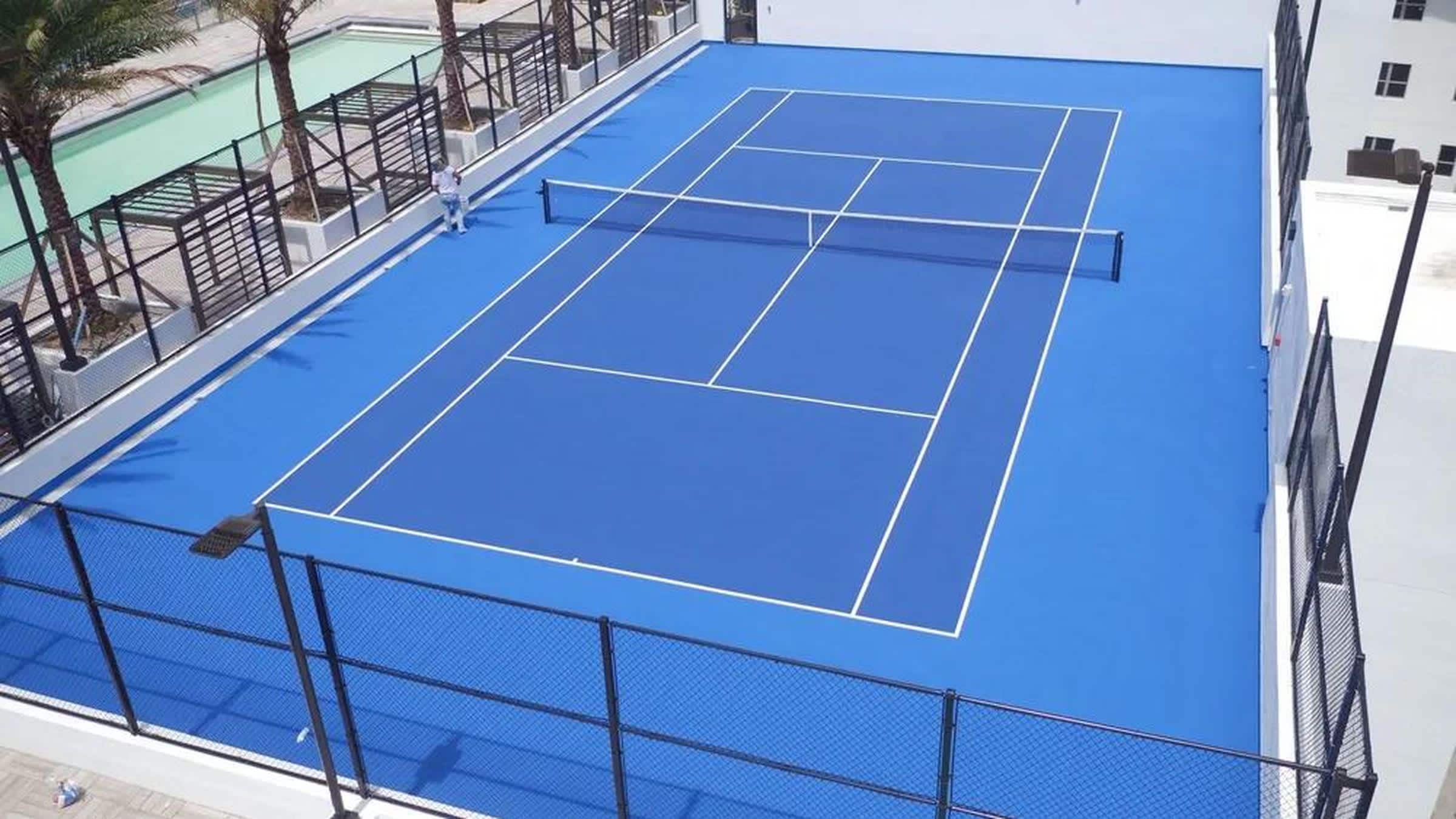 Un campo da tennis con superficie blu e linee bianche, circondato da una recinzione nera.
