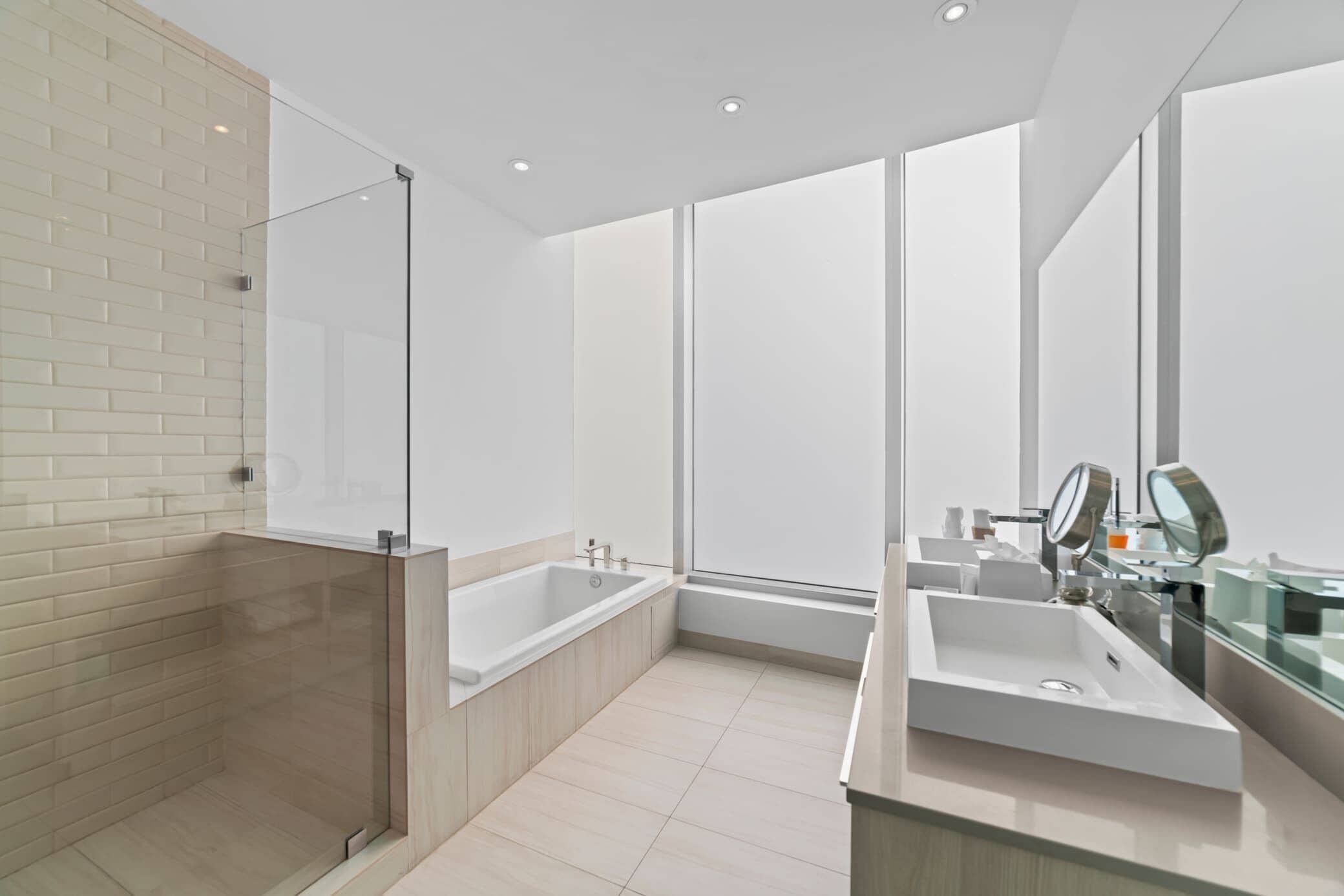 Un baño moderno con ducha envuelta en cristal, una bañera independiente, un espejo grande y un lavabo con encimera.