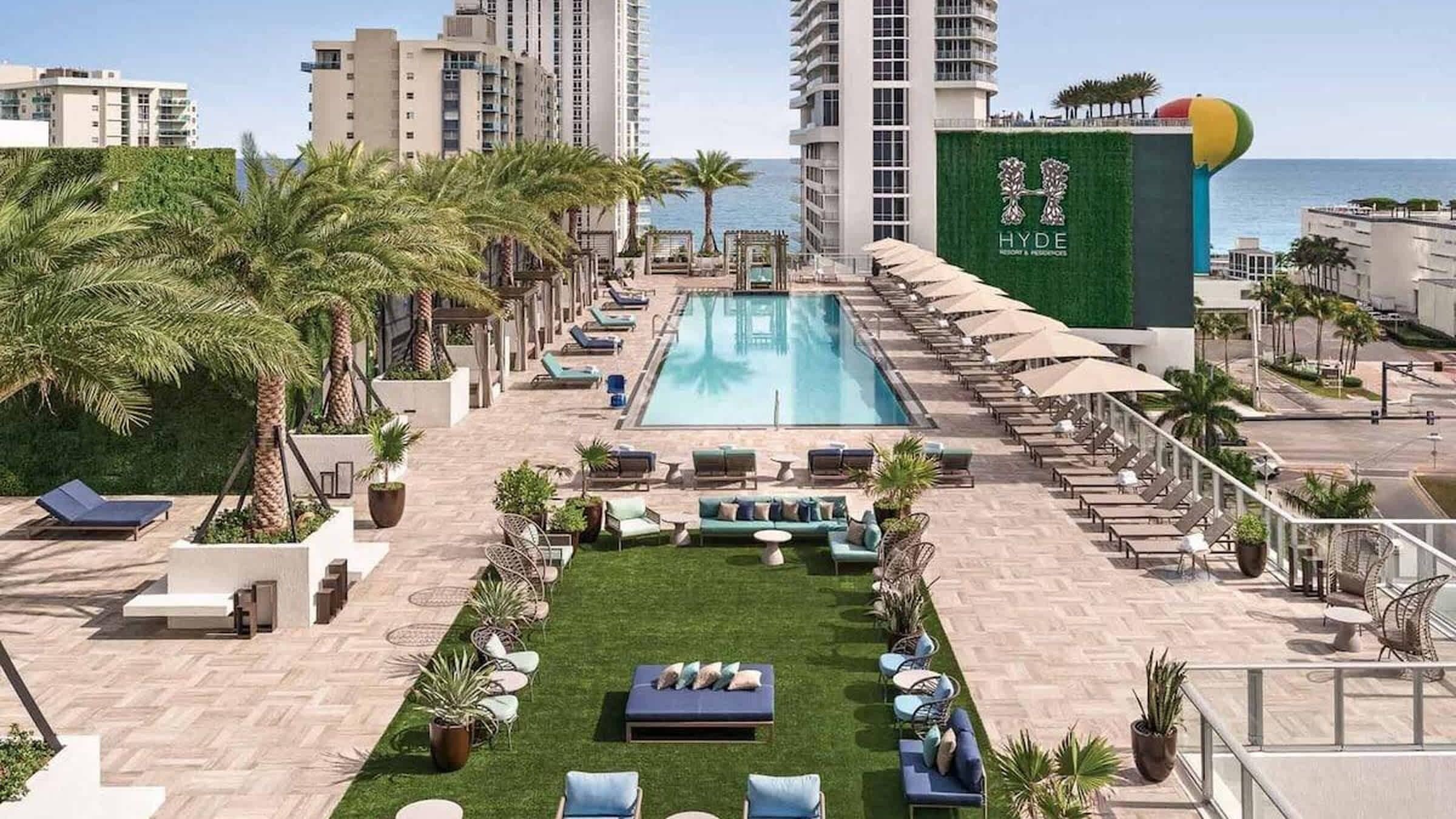 A hotel pool area with lounge chairs, a small lawn, and a view of the sea.