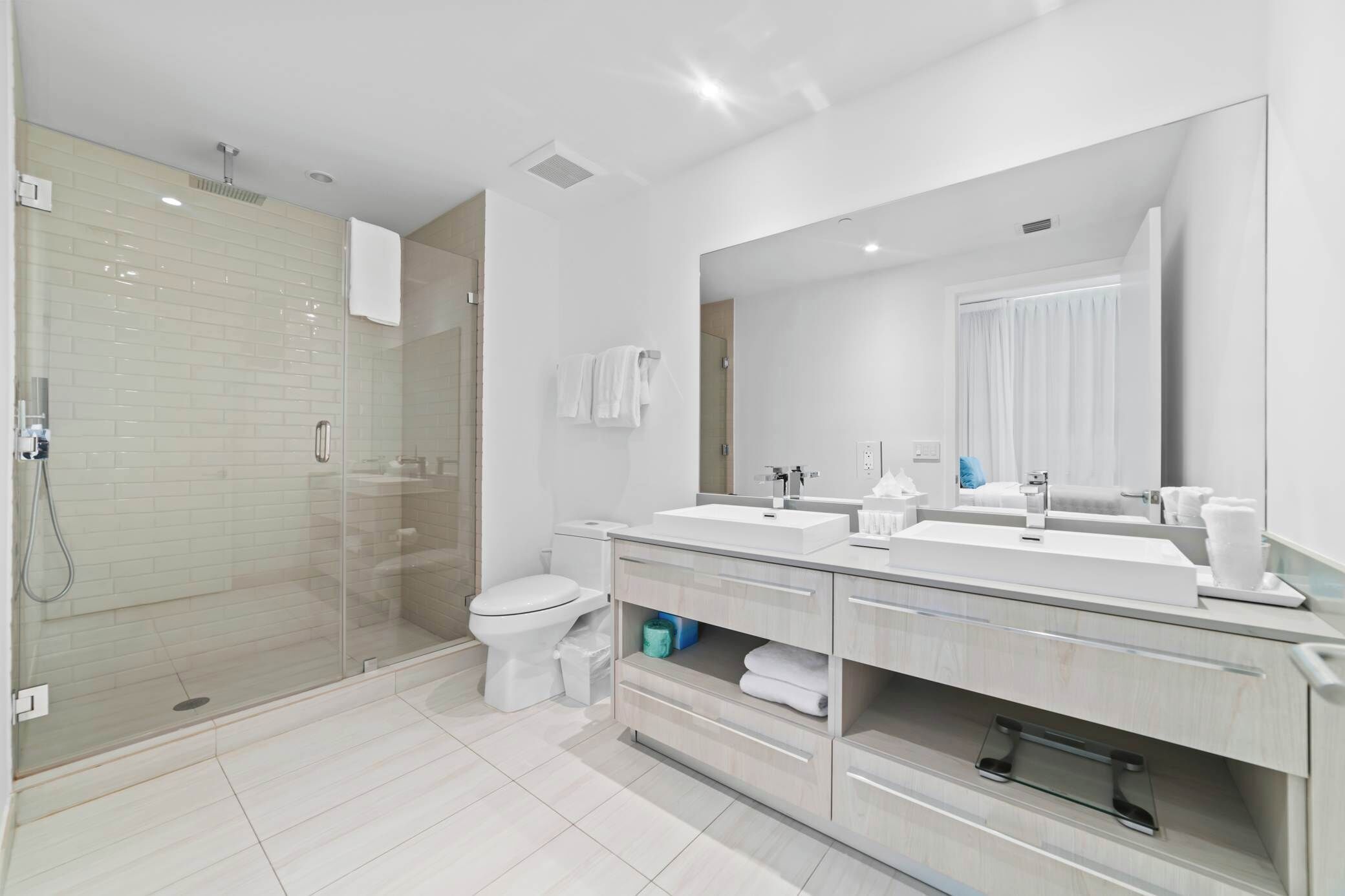 A modern bathroom with a glass-enclosed shower, a white toilet, and a double sink vanity with a large mirror.