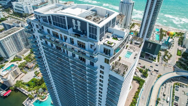 A high-rise hotel with a rooftop pool, a view of the ocean, and a parking area. - 2BR Ocean Penthouse: Private Terrace & Hot Tub (Hollywood)