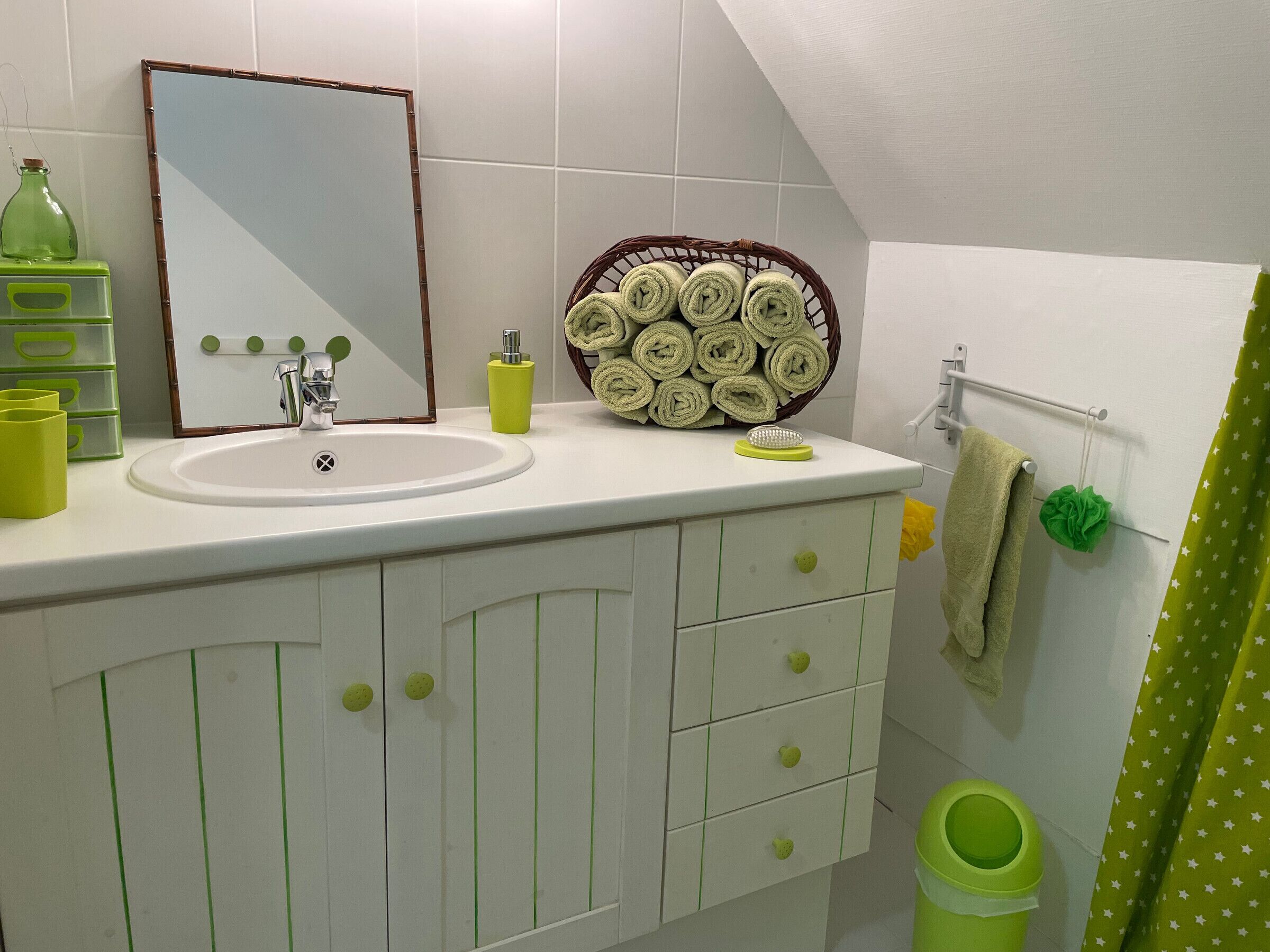 A bathroom with a sink, mirror, green storage drawers, a basket of towels, and a green trash bin.