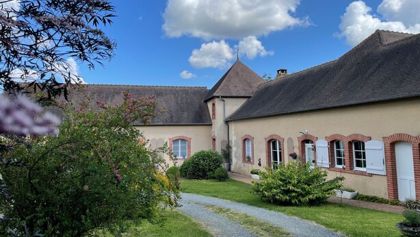 Un bâtiment traditionnel avec un toit en tuiles, un chemin de gravier et un jardin bien entretenu.