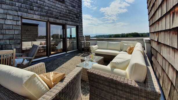 Eine Dachterrasse mit Korbmöbeln, einem Glastisch und Blick auf die Landschaft.