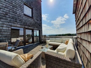 Eine Dachterrasse mit Korbmöbeln, einem Glastisch und Blick auf die Landschaft.