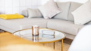 Ein Wohnzimmer mit einem runden Glastisch, einem beigen Sofa und einer gelben Decke.