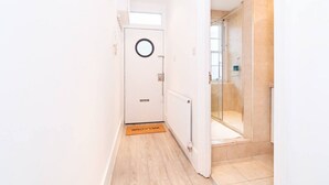 A hallway with a white door, a welcome mat, and a glass shower area. - New 2Bed apartment in Covent Garden (London)
