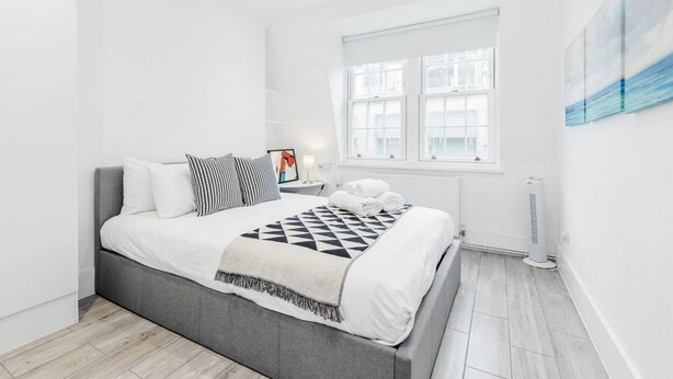 A modern bedroom with a grey bed, white bedding, and a geometric-patterned throw. - New 2Bed apartment in Covent Garden (London)