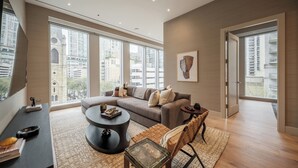 Ein modernes Wohnzimmer mit einer Eckcouch, einem runden Couchtisch, einem Esstisch mit Glasplatte und einem großen Fenster mit Blick auf die Stadt.