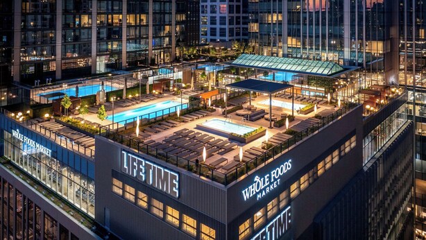 Ein Poolbereich auf dem Dach mit Liegestühlen und Sonnenschirmen, umgeben von Gebäuden mit 'Whole Foods Market'-Beschriftung.