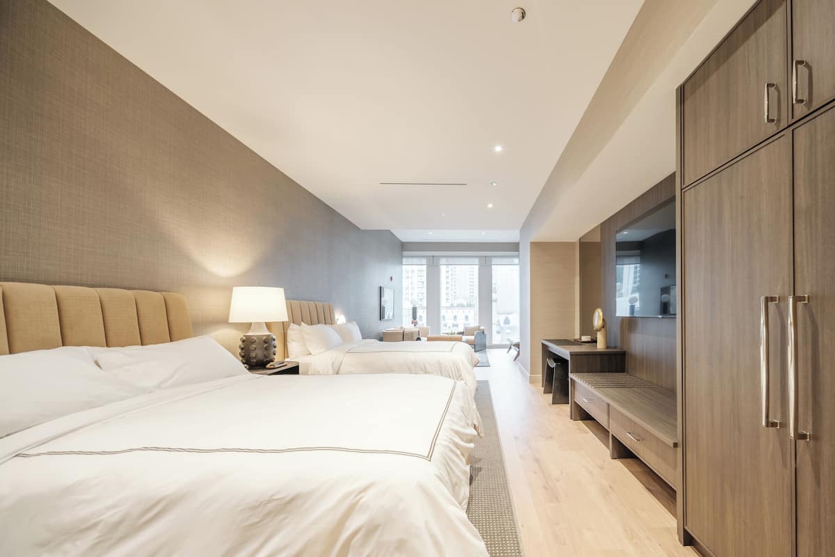Ein modernes Hotelzimmer mit zwei Betten, einem Schreibtisch, einem Fernseher und einem Kleiderschrank.