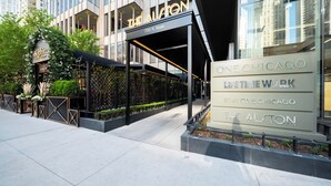 Ein moderner Hotelzugang mit Glasfassade, einem überdachten Außenbereich zum Sitzen und Beschilderung für 'The Alston' und 'One Chicago Life Time Work'.