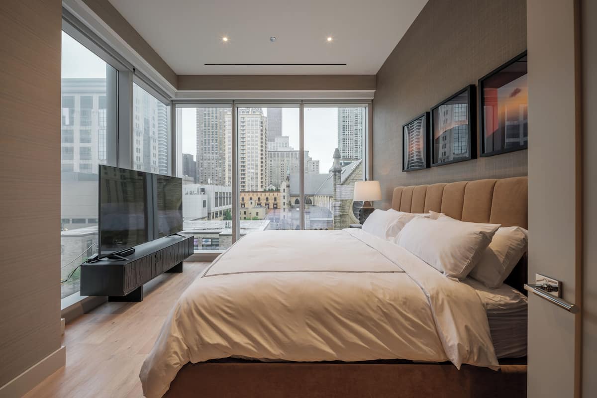 Ein modernes Schlafzimmer mit einem großen Bett, einem Fernseher und Blick auf die Stadt.