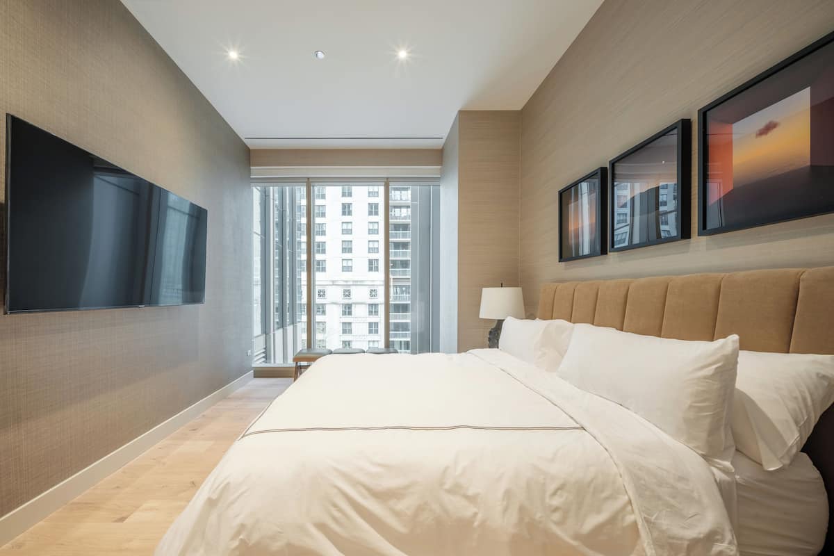 Ein modernes Hotelzimmer mit einem großen Bett, einem wandmontierten Flachbildfernseher und Blick auf die Stadt durch große Fenster.