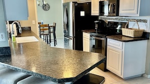 A modern kitchen with a central island, stainless steel appliances, and a ceiling fan. - 3-bedroom & den house in welcoming Cape Coral with Pool, centrally located!🌴 (Cape Coral)